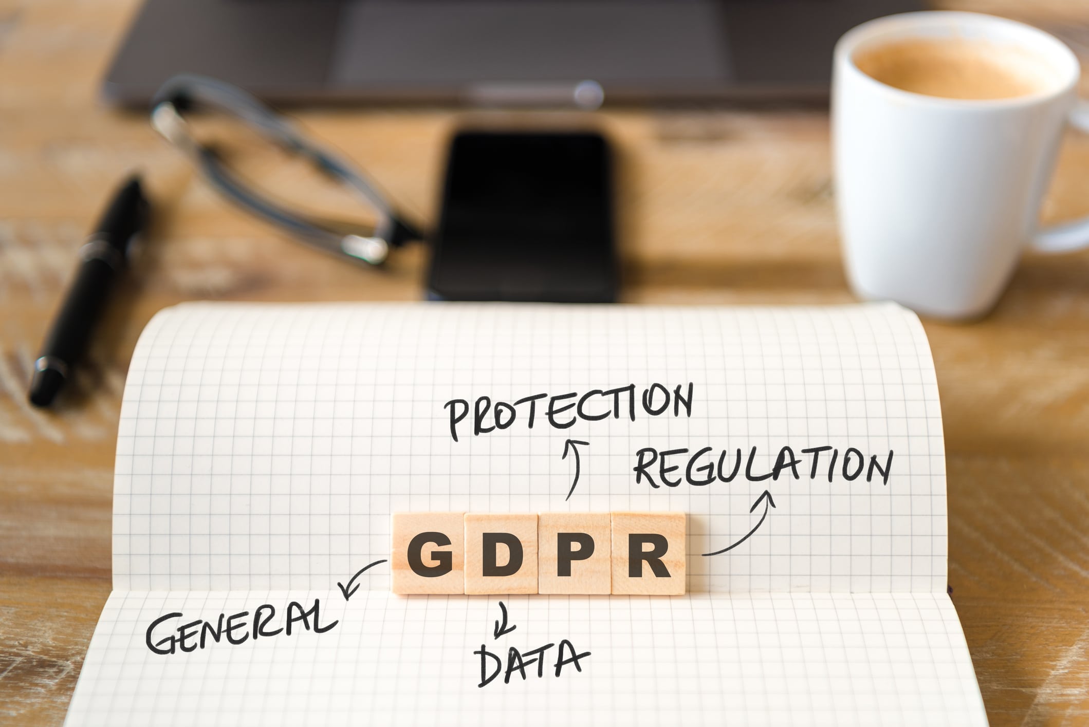 Closeup on notebook over wood table background, focus on wooden blocks with letters making GDPR General Data Protection Regulation text
